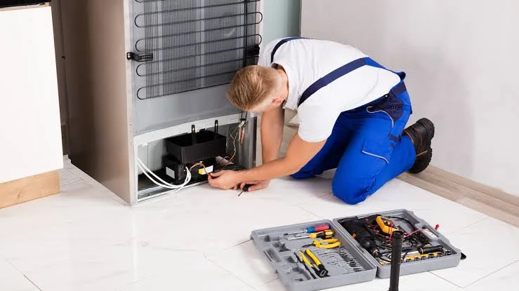 Technician inspecting the compressor area behind a refrigerator