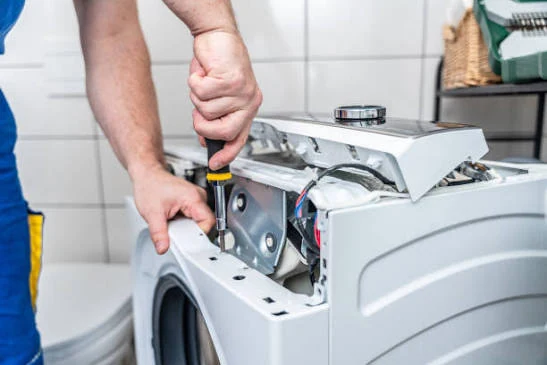 Hands using a screwdriver on an opened washing machine control panel